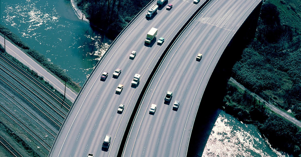 An aerial view of vehicles on a freeway bridge passing over a river.
