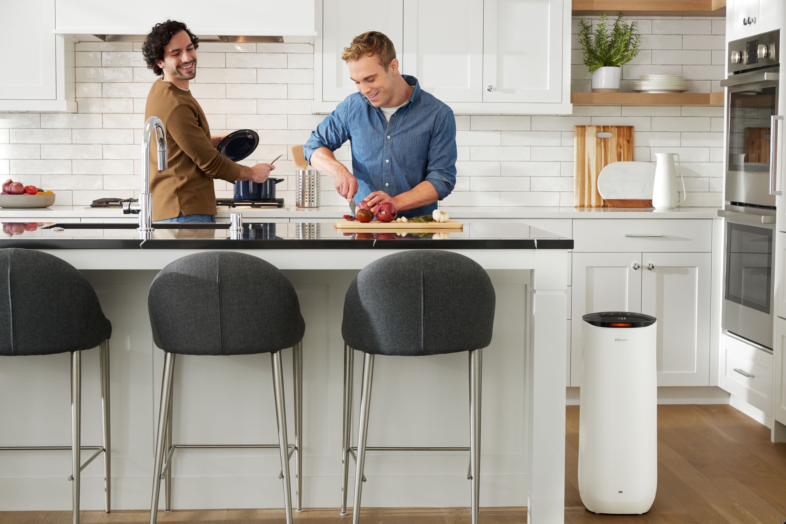Air purifier positioned by two men preparing a meal in the kitchen.