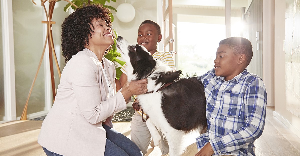 Mother and two children kneeling on floor while greeting dog.